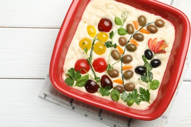 Photo of Raw focaccia with vegetables and olives in baking dish on white wooden table, top view. Space for text