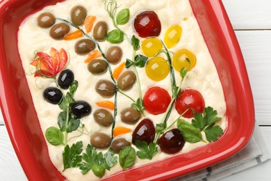 Photo of Raw focaccia with vegetables and olives in baking dish on white wooden table, top view
