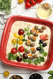 Photo of Raw focaccia with vegetables, olives and spices on white wooden table, flat lay