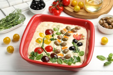 Photo of Raw focaccia with vegetables, olives and spices on white wooden table, closeup