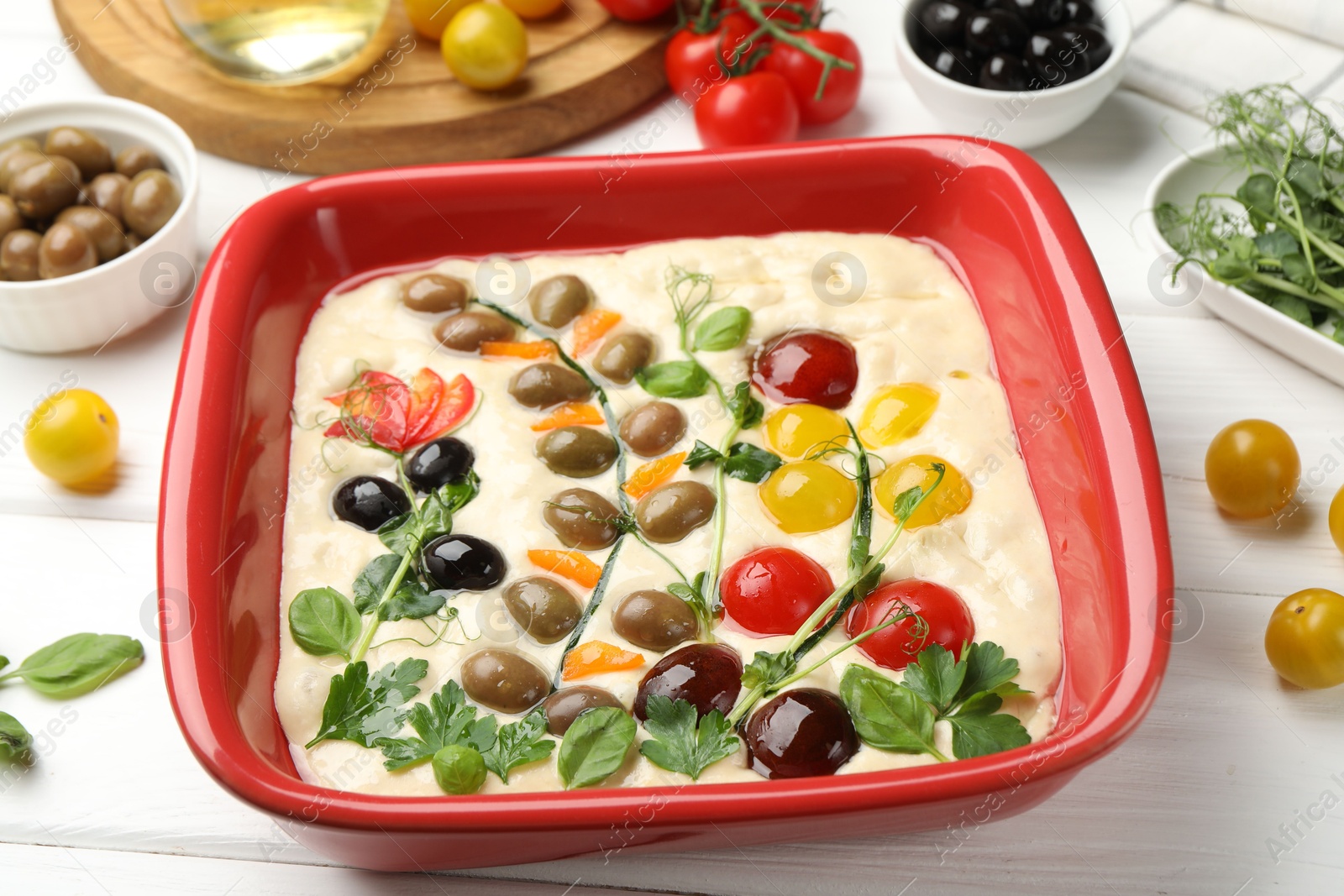 Raw focaccia with vegetables, olives and spices on white wooden table, closeup Photo of Raw focaccia with vegetables, olives and spices on white wooden table, closeup