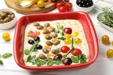 Photo of Raw focaccia with vegetables, olives and spices on white wooden table, closeup
