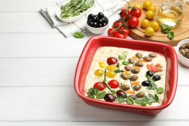 Photo of Raw focaccia with vegetables, olives and spices on white wooden table, closeup. Space for text