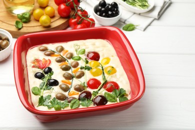Photo of Raw focaccia with vegetables, olives and spices on white wooden table, closeup. Space for text