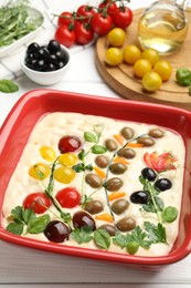 Photo of Raw focaccia with vegetables, olives and spices on white wooden table, closeup