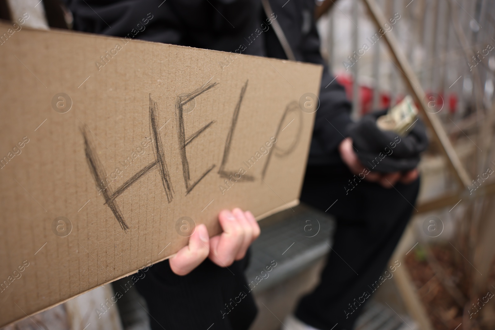 Homeless man holding sign with word Help and money outdoors, selective focus Photo of Homeless man holding sign with word Help and money outdoors, selective focus