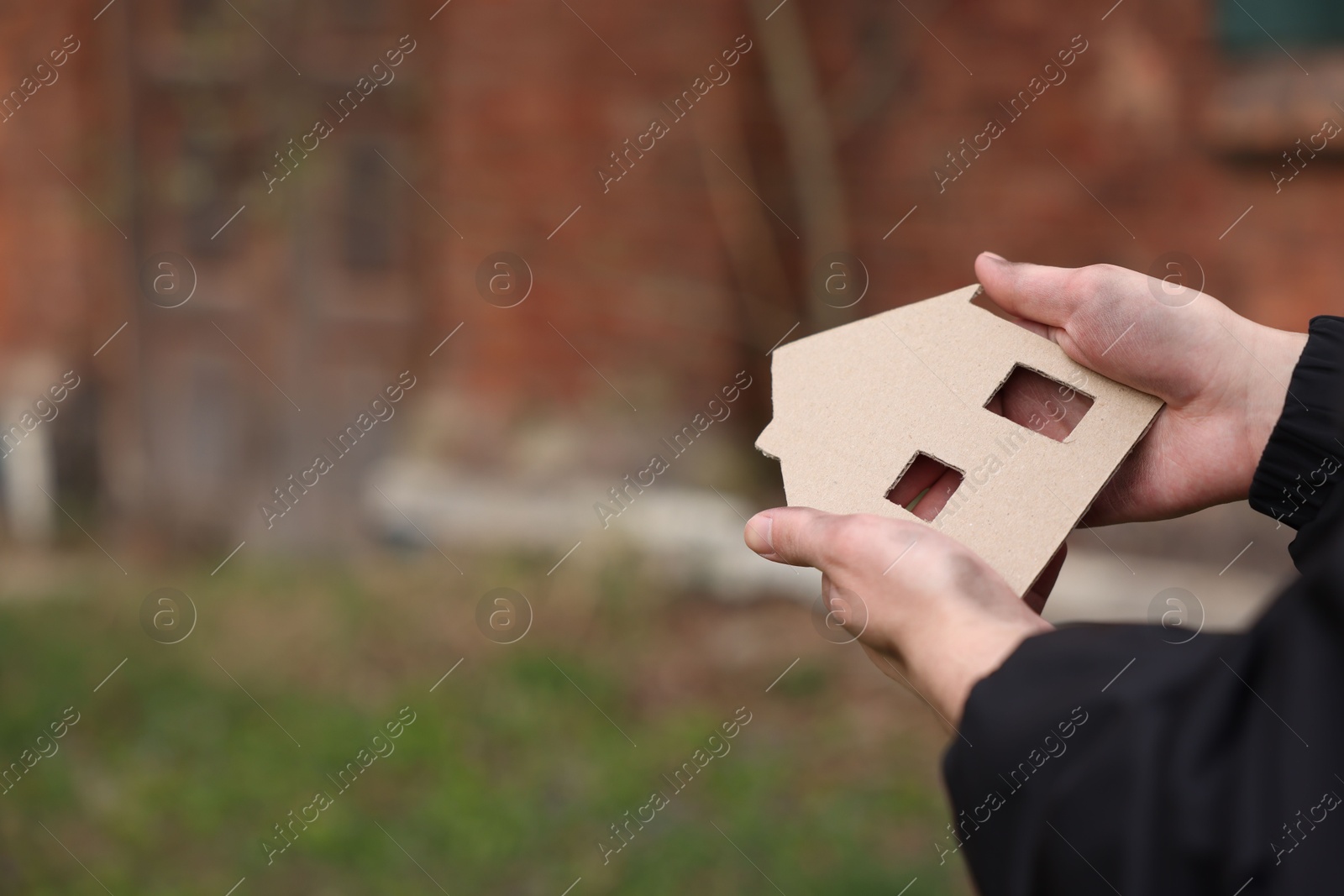 Homeless man with carton house figure outdoors, closeup. Space for text Photo of Homeless man with carton house figure outdoors, closeup. Space for text