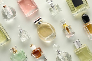 Photo of Bottles of various perfumes on light background, flat lay