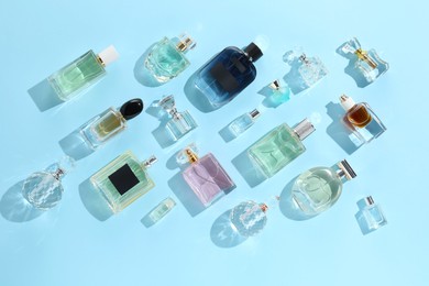 Photo of Bottles of various perfumes on light blue background, flat lay