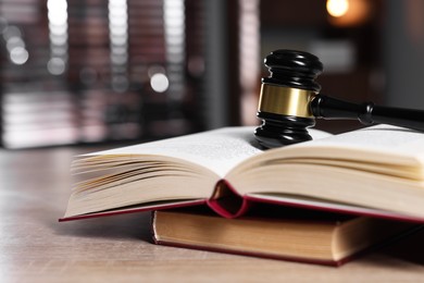 Photo of Judge's gavel and books on wooden table against blurred background, closeup