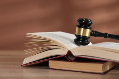 Photo of Judge's gavel and books on wooden table against brown background, closeup