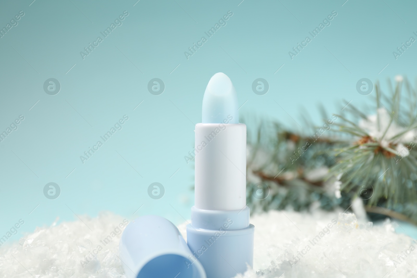Moisturizing lip balm and fir tree branches on artificial snow against light blue background, closeup. Winter care Photo of Moisturizing lip balm and fir tree branches on artificial snow against light blue background, closeup. Winter care