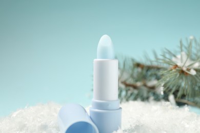 Photo of Moisturizing lip balm and fir tree branches on artificial snow against light blue background, closeup. Winter care