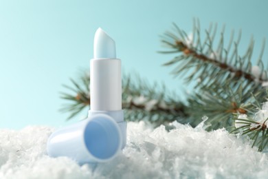 Photo of Moisturizing lip balm and fir tree branches on artificial snow against light blue background, closeup. Winter care