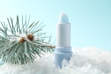 Photo of Moisturizing lip balm and fir tree branches on artificial snow against light blue background, closeup. Winter care
