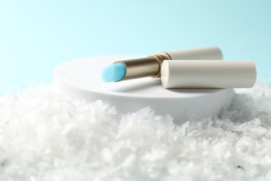 Photo of Moisturizing lip balm on artificial snow against light blue background, closeup. Winter care