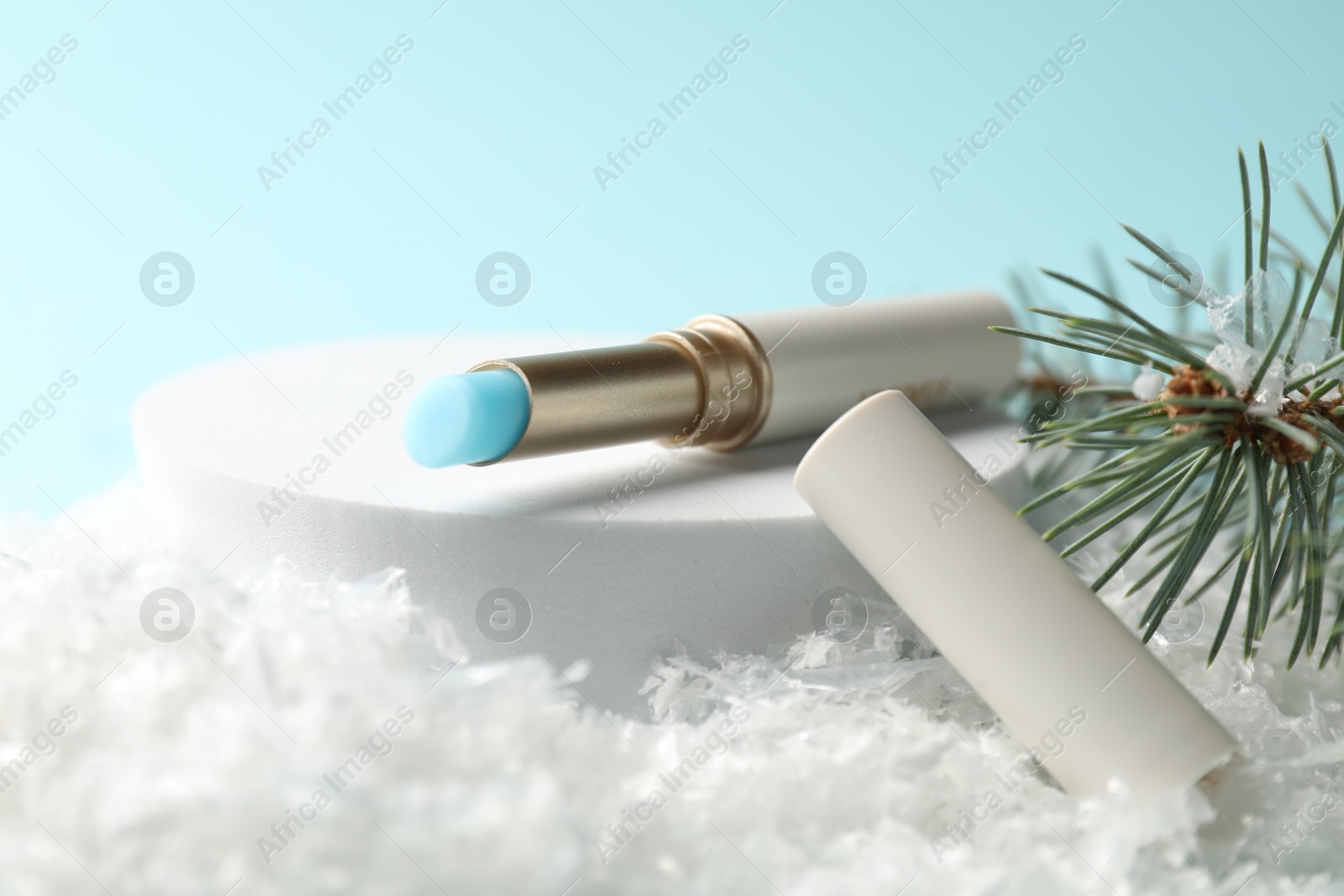 Moisturizing lip balm and fir tree branches on artificial snow against light blue background, closeup. Winter care Photo of Moisturizing lip balm and fir tree branches on artificial snow against light blue background, closeup. Winter care