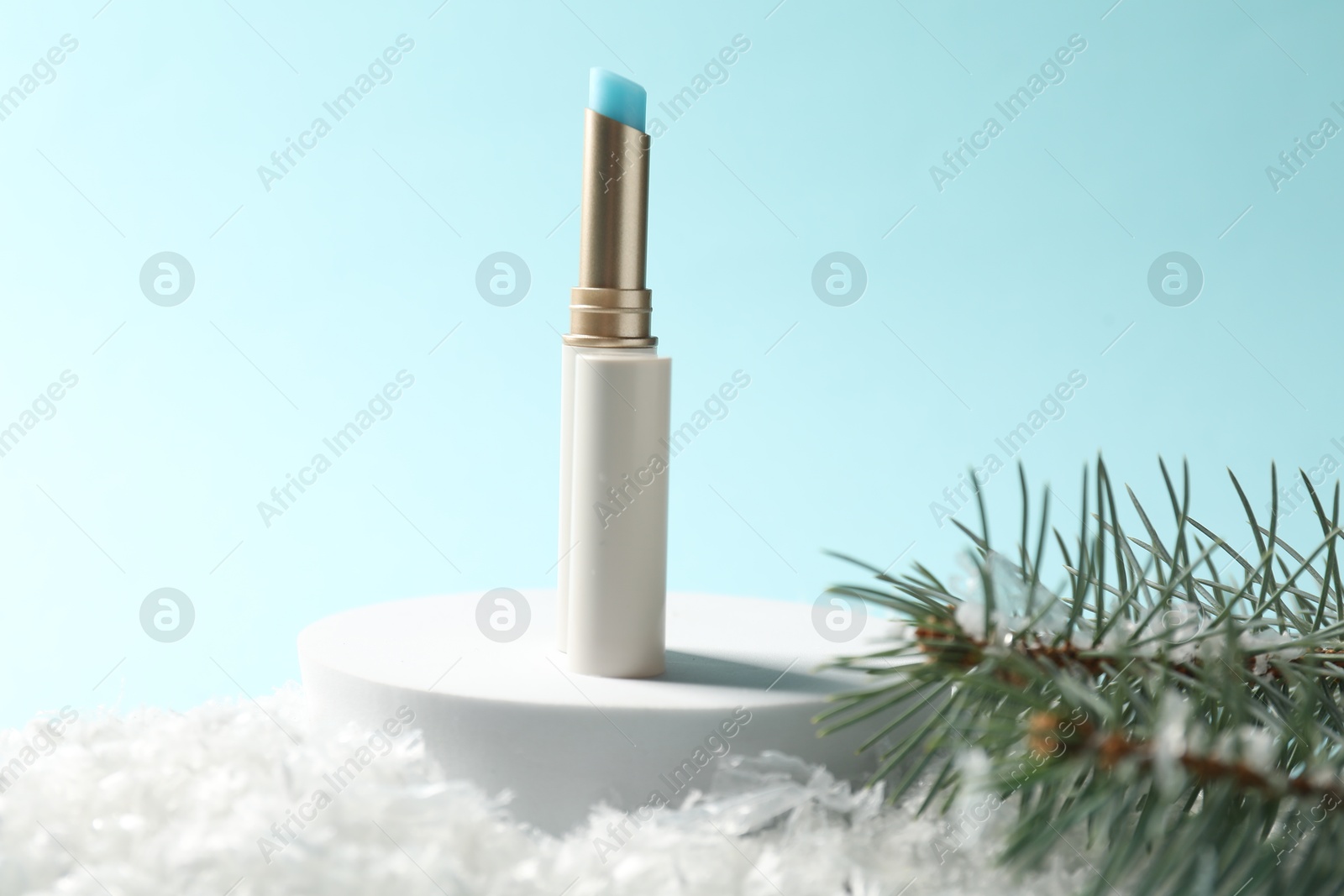Moisturizing lip balm and fir tree branches on artificial snow against light blue background, closeup. Winter care Photo of Moisturizing lip balm and fir tree branches on artificial snow against light blue background, closeup. Winter care
