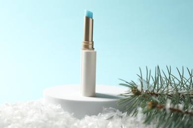 Photo of Moisturizing lip balm and fir tree branches on artificial snow against light blue background, closeup. Winter care