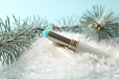 Photo of Moisturizing lip balm and fir tree branches on artificial snow against light blue background, closeup. Winter care