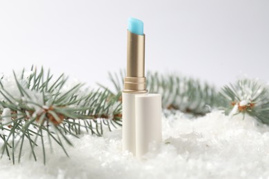 Photo of Moisturizing lip balm and fir tree branches on artificial snow against white background, closeup. Winter care