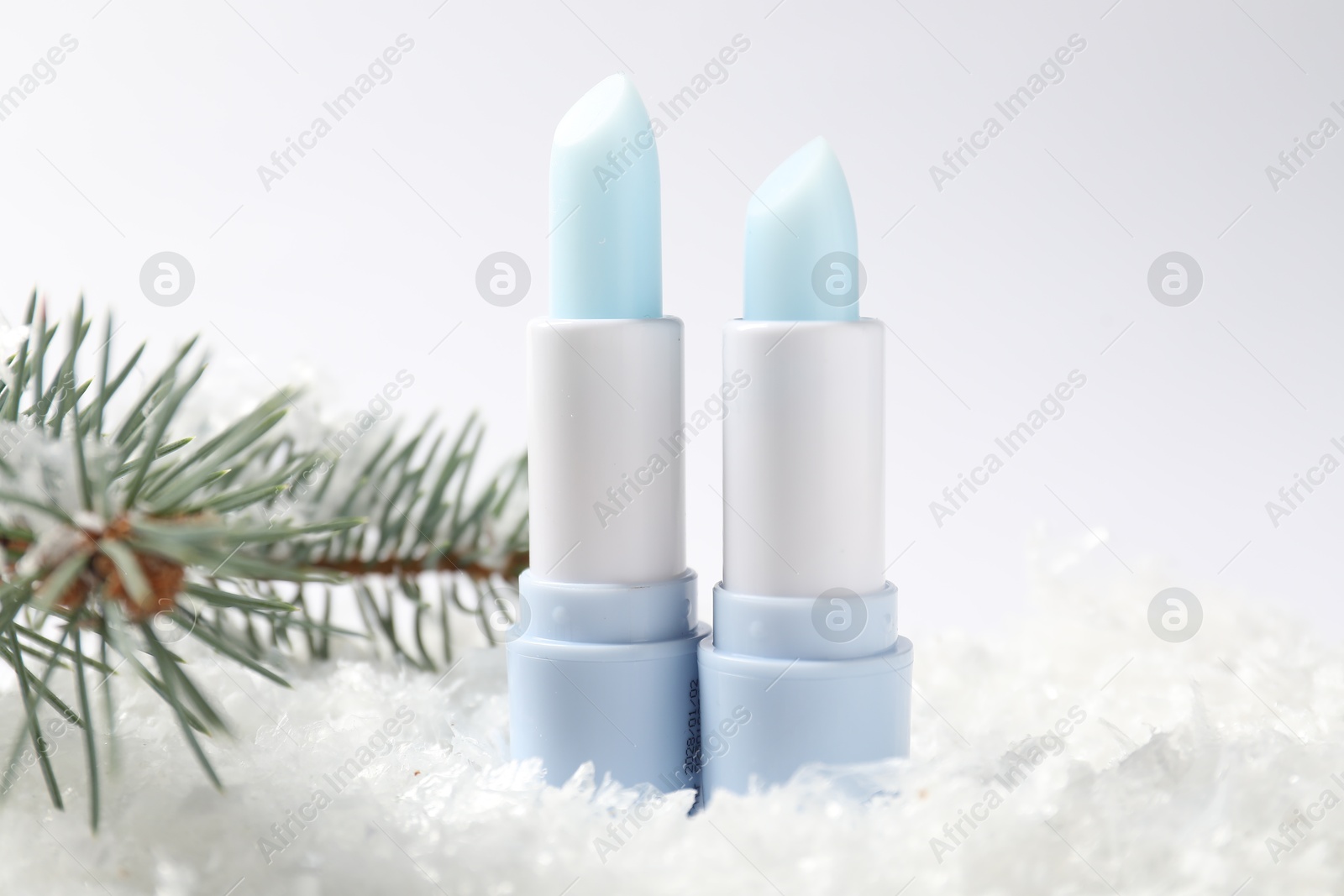 Moisturizing lip balms and fir tree branches on artificial snow against white background, closeup. Winter care Photo of Moisturizing lip balms and fir tree branches on artificial snow against white background, closeup. Winter care