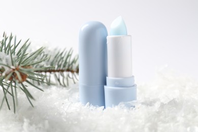 Photo of Moisturizing lip balms and fir tree branches on artificial snow against white background, closeup. Winter care