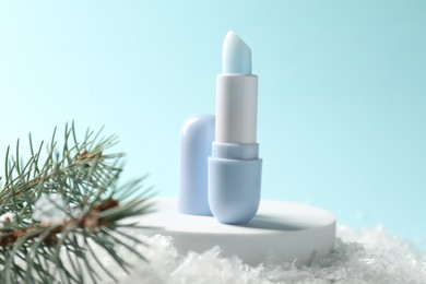 Photo of Moisturizing lip balm and fir tree branches on artificial snow against light blue background, closeup. Winter care