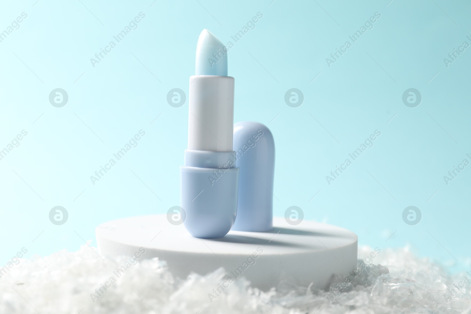 Moisturizing lip balm on artificial snow against light blue background, closeup. Winter care Photo of Moisturizing lip balm on artificial snow against light blue background, closeup. Winter care