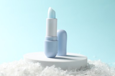 Photo of Moisturizing lip balm on artificial snow against light blue background, closeup. Winter care