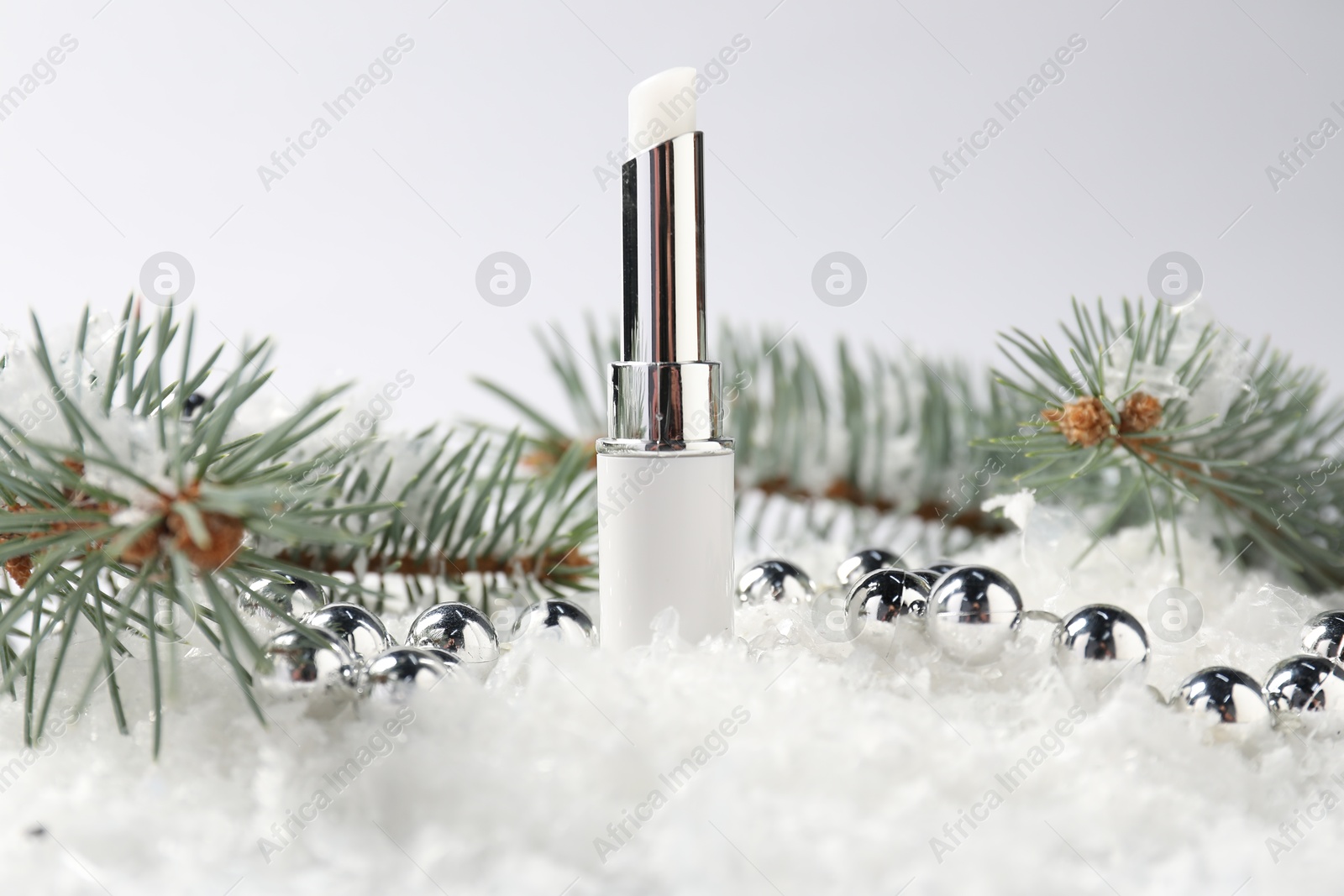 Moisturizing lip balm, Christmas decor and fir tree branches on artificial snow against white background, closeup. Winter care Photo of Moisturizing lip balm, Christmas decor and fir tree branches on artificial snow against white background, closeup. Winter care