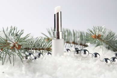 Photo of Moisturizing lip balm, Christmas decor and fir tree branches on artificial snow against white background, closeup. Winter care