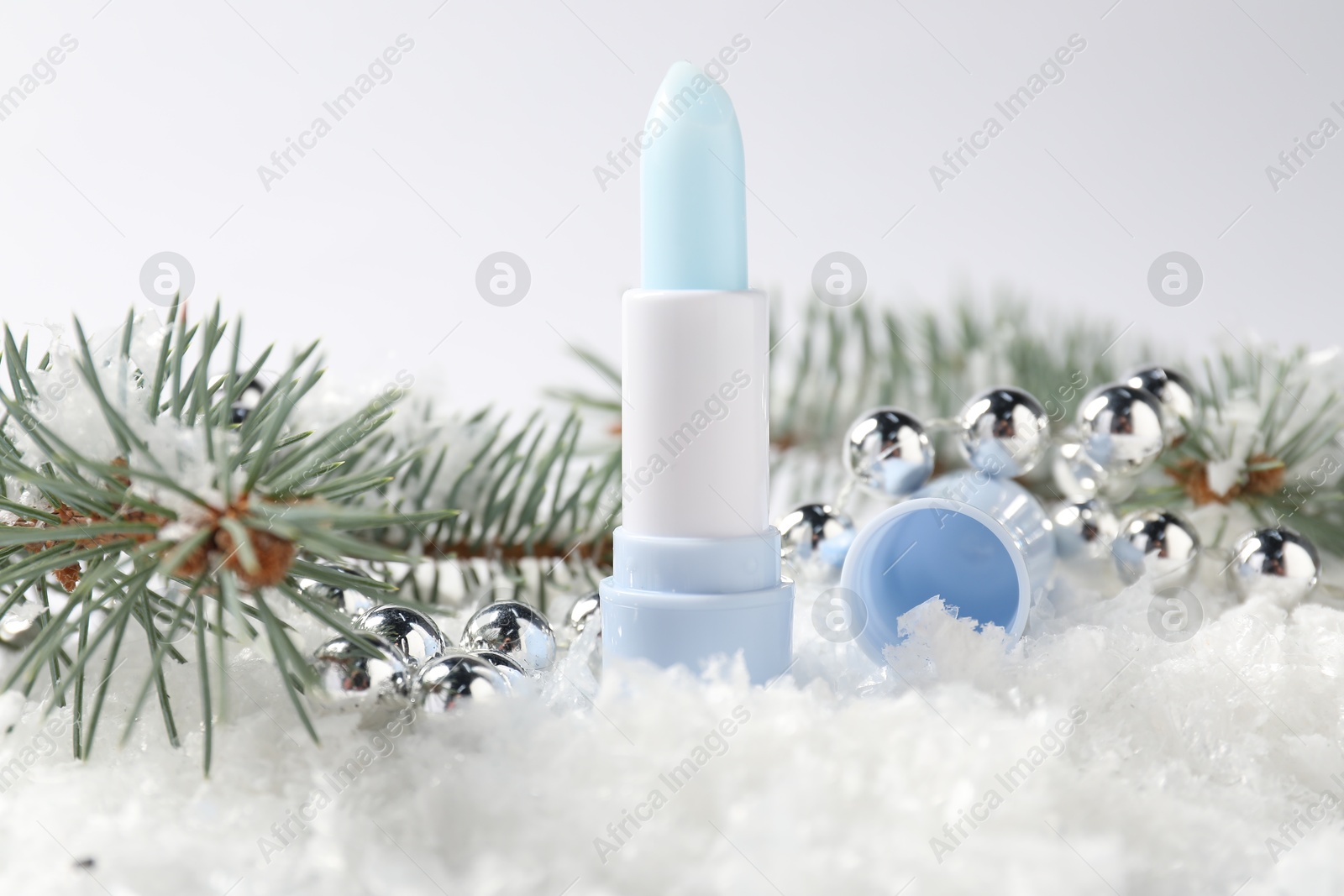 Moisturizing lip balm, Christmas decor and fir tree branches on artificial snow against white background, closeup. Winter care Photo of Moisturizing lip balm, Christmas decor and fir tree branches on artificial snow against white background, closeup. Winter care