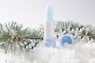 Photo of Moisturizing lip balm, Christmas decor and fir tree branches on artificial snow against white background, closeup. Winter care