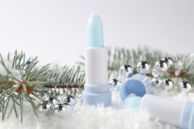 Photo of Moisturizing lip balms, Christmas decor and fir tree branches on artificial snow against white background, closeup. Winter care