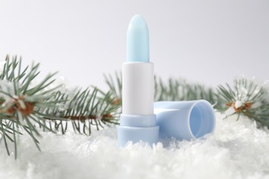 Photo of Moisturizing lip balm and fir tree branches on artificial snow against white background, closeup. Winter care