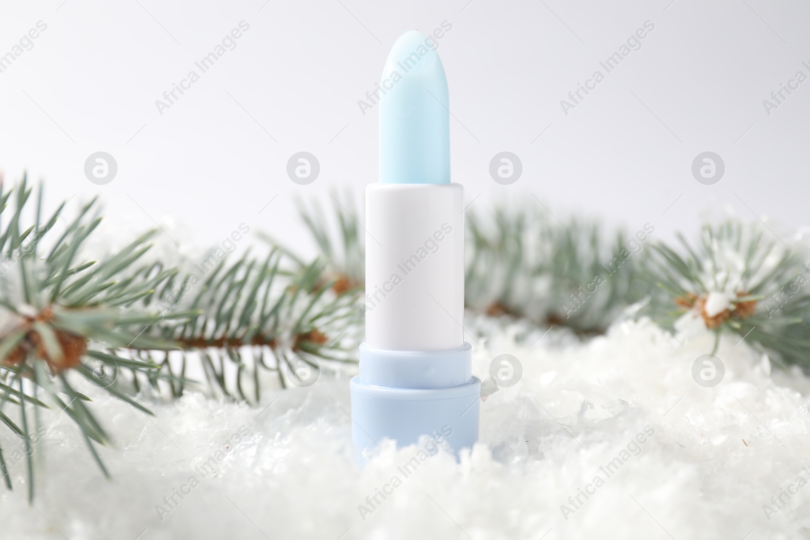 Moisturizing lip balm and fir tree branches on artificial snow against white background, closeup. Winter care Photo of Moisturizing lip balm and fir tree branches on artificial snow against white background, closeup. Winter care