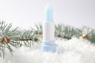 Photo of Moisturizing lip balm and fir tree branches on artificial snow against white background, closeup. Winter care