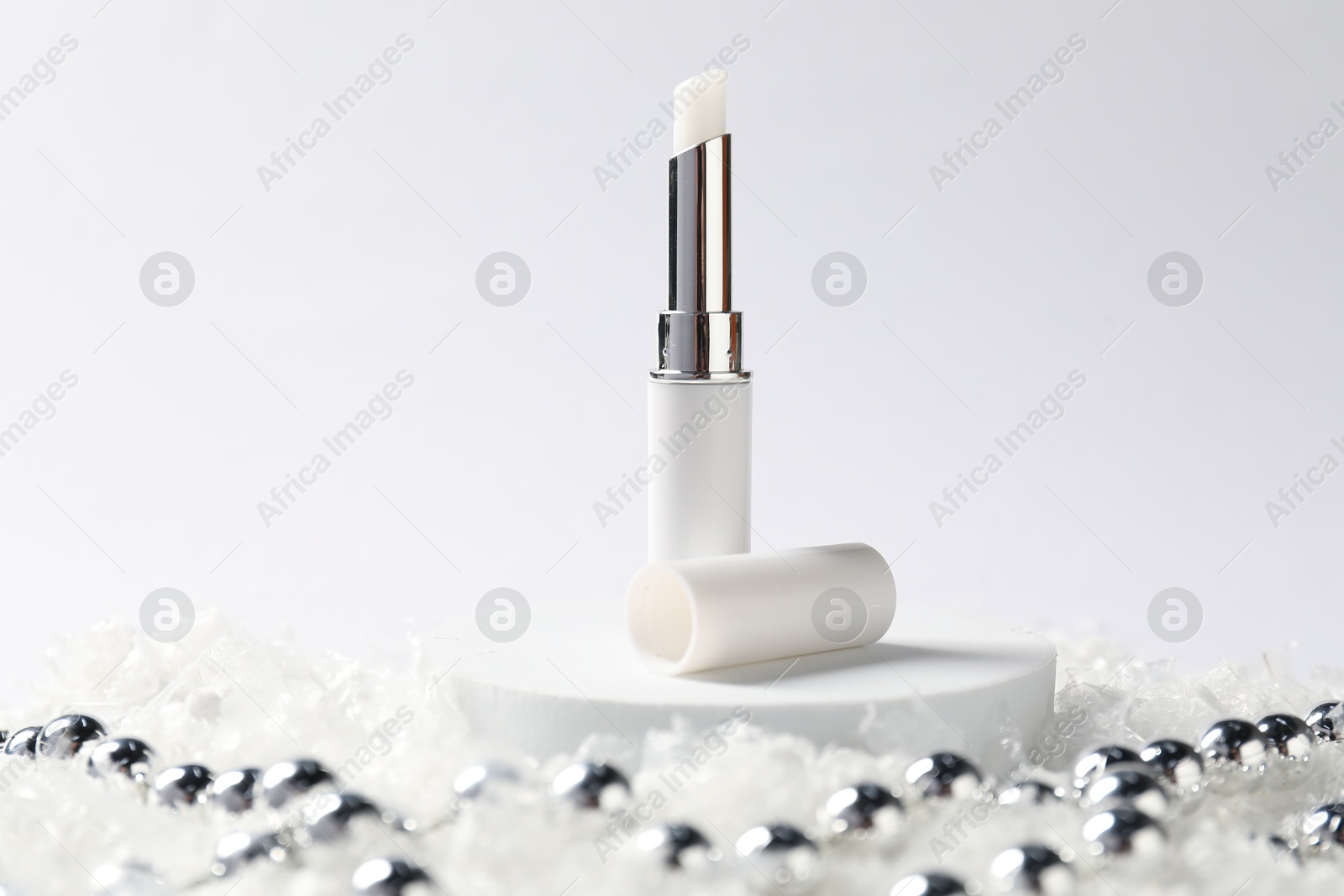 Moisturizing lip balm and Christmas decor on artificial snow against white background, closeup. Winter care Photo of Moisturizing lip balm and Christmas decor on artificial snow against white background, closeup. Winter care