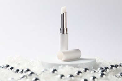 Photo of Moisturizing lip balm and Christmas decor on artificial snow against white background, closeup. Winter care