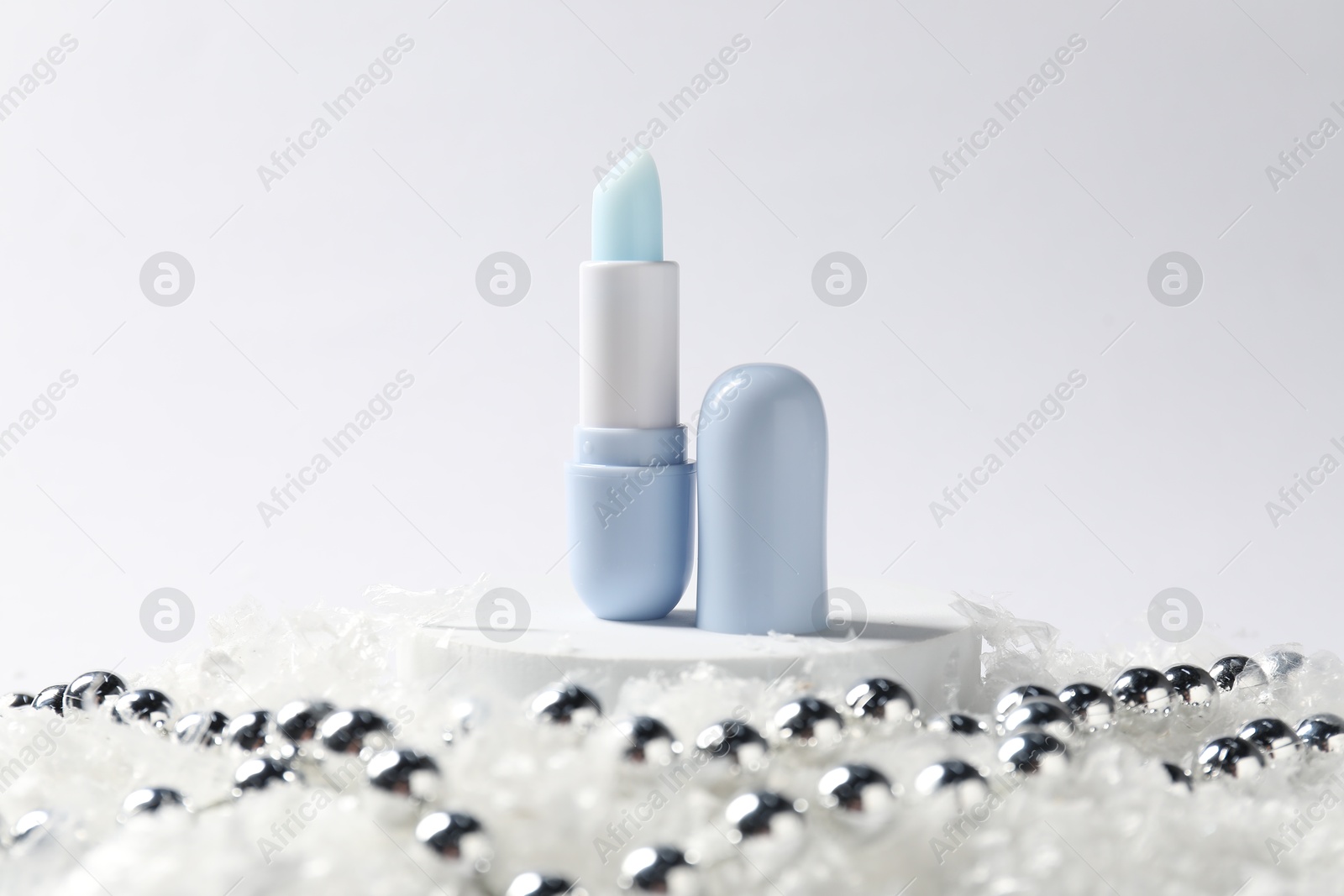 Moisturizing lip balm and Christmas decor on artificial snow against white background, closeup. Winter care Photo of Moisturizing lip balm and Christmas decor on artificial snow against white background, closeup. Winter care