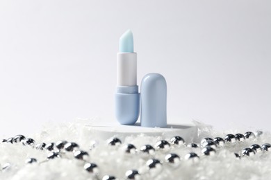 Photo of Moisturizing lip balm and Christmas decor on artificial snow against white background, closeup. Winter care