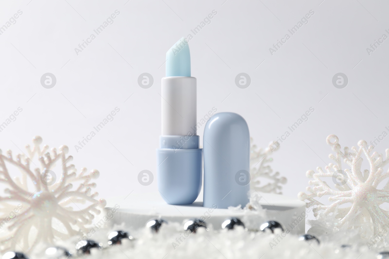 Moisturizing lip balm and Christmas decor on artificial snow against white background, closeup. Winter care Photo of Moisturizing lip balm and Christmas decor on artificial snow against white background, closeup. Winter care