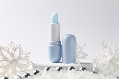 Photo of Moisturizing lip balm and Christmas decor on artificial snow against white background, closeup. Winter care