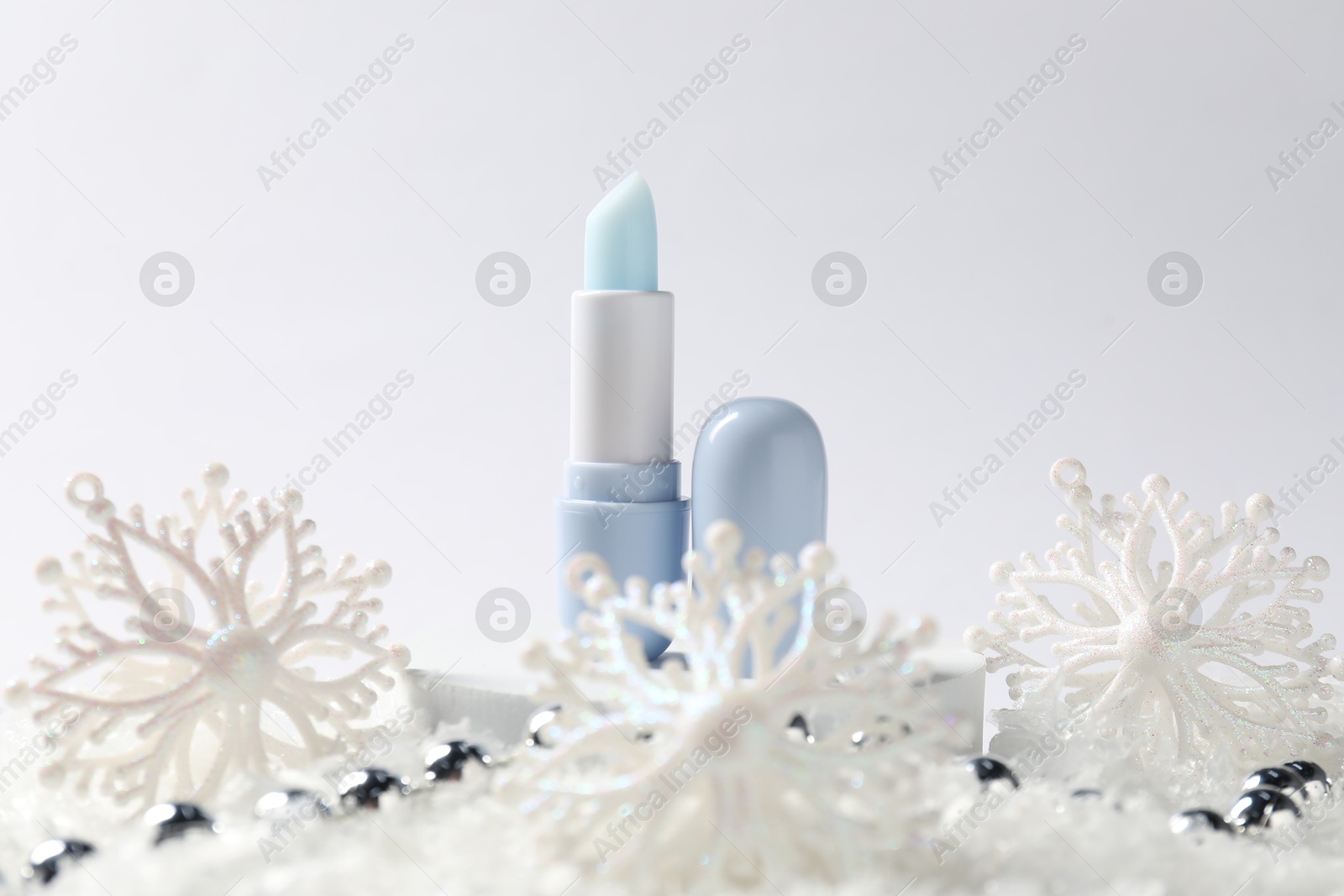 Moisturizing lip balm and Christmas decor on artificial snow against white background, closeup. Winter care Photo of Moisturizing lip balm and Christmas decor on artificial snow against white background, closeup. Winter care