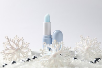 Photo of Moisturizing lip balm and Christmas decor on artificial snow against white background, closeup. Winter care