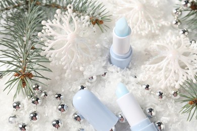 Photo of Moisturizing lip balm, Christmas decor and fir tree branches on artificial snow, closeup. Winter care