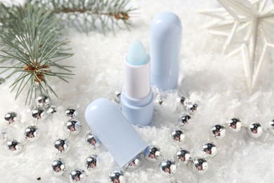 Photo of Moisturizing lip balm, Christmas decor and fir tree branches on artificial snow, closeup. Winter care