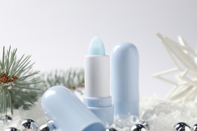 Photo of Moisturizing lip balms, Christmas decor and fir tree branches on artificial snow against white background, closeup. Winter care