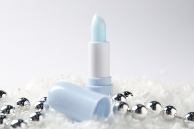 Photo of Moisturizing lip balm and Christmas decor on artificial snow against white background, closeup. Winter care